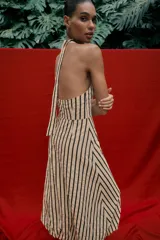 Vestido midi de corte globo con estampado de rayas verticales, cuello halter anudado, escote en pico y espalda descubierta. Presenta bajo abullonado con elástico interior y cierre lateral con cremallera oculta.