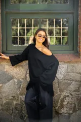 Buzo de punto color negro, con diseño oversize, cuello redondo y mangas largas. Presenta un detalle de flecos en el ruedo inferior que aporta movimiento a la prenda.