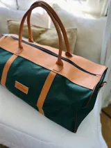 Bolso de lona color verde militar con detalles en cuero marrón. Tiene doble asa de mano y correa de hombro ajustable y extraíble.