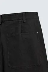 Pantalón wide fit de algodón con efecto lavado, corte recto y holgado. Presenta un cierre frontal cruzado con botones y un alamar metálico distintivo, además de bolsillos frontales y traseros de plastrón.