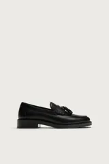 Mocasín de vestir color negro, con diseño de antifaz en el empeine y detalle de borlas. Presenta una horma redonda y suela a tono.