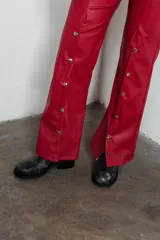 Pantalón de cuero sintético color rojo, de tiro alto y corte acampanado, con bolsillos delanteros y traseros, y botones metálicos a lo largo de la pierna.