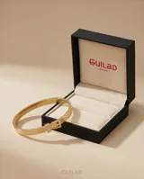 Esclava rígida de acero con baño de oro, con textura grabada y detalle de hebilla decorativa con incrustaciones de circonias.