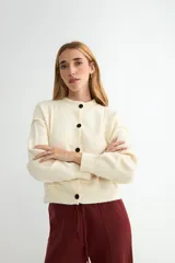Cardigan de punto color crema, con cuello redondo, manga larga y cierre frontal con botones negros en contraste.