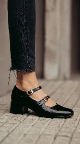 Zapatos tipo Mary Jane de cuero negro con acabado brillante, diseño de doble tira con hebillas metálicas y taco cuadrado bajo.