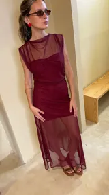 Vestido largo de microtul bordó, sin mangas, con escote alto tipo buche y diseño transparente con forro corto interno que genera un efecto translúcido en la falda.