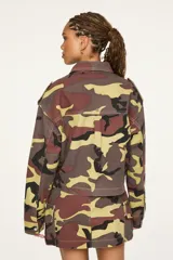 Chaqueta de denim con estampado camuflado en tonos marrón, verde y beige, de corte recto y largo recortado. Cuenta con cuello camisero, cierre frontal con cremallera, bolsillos con solapa en el pecho y solapas decorativas en los hombros.