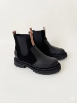 Botas tipo chelsea de cuero, combinando texturas en color bordó. Presentan paneles laterales elásticos en negro, suela track robusta y tiradores en la parte superior.