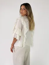 Blusa blanca de manga corta abullonada con volados en cascada y cierre delantero con cordones para atar.