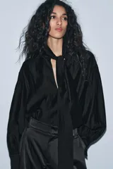 Camisa fluida de cuello redondo con escote en pico y lazada frontal en el mismo tejido. Presenta mangas largas con puños anchos y bajo recto.