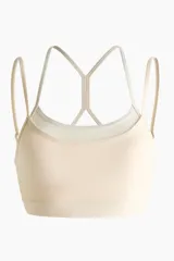 Top deportivo color beige claro con dos pares de tirantes finos en contraste y diseño de espalda cruzada.