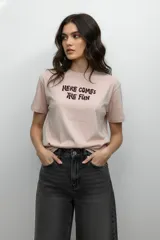 Remera de algodón color rosado, de corte holgado y manga corta, con cuello redondo y estampado frontal con la frase 'Here comes the fun'.