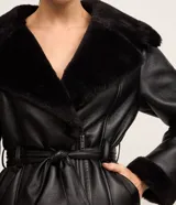 Blazer negro confeccionado en material sintético PU, con cuello y puños de piel sintética, cierre por cremallera y cinturón con hebilla en la cintura.