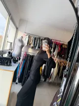 Vestido largo negro de corte ajustado, con mangas largas acampanadas y detalle de nudo frontal en la cintura que crea un efecto drapeado.
