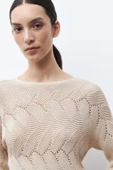 Sweater de punto color beige claro, con escote bote y tejido calado con diseño ondulado. Es de manga larga y corte recto.