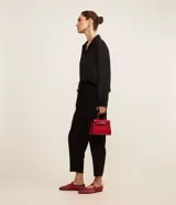 Pantalón de crepé rojo, modelo estilo pijama, de corte fluido, con cintura elástica y lazo de ajuste con terminales metálicas. Cuenta con bolsillos laterales y cierre frontal con cremallera y botón.