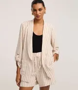 Blazer de poliéster color crudo con rayas verticales finas en marrón. Tiene cuello con solapas peaked, bolsillos delanteros y mangas largas con botón para arremangar. Sin forro.