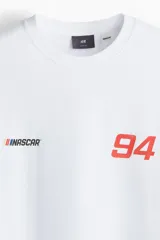 Remera blanca de corte holgado con hombros caídos y cuello redondo. Presenta estampado pequeño de NASCAR y el número 94 en el pecho.