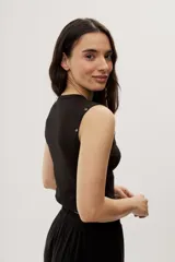 Top crop negro de calce ajustado, con escote redondo, diseño sin mangas y detalles de ojales metálicos decorativos en los hombros.