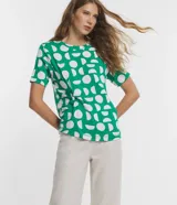 Blusa de viscosa con cuello redondo, manga corta y diseño con nudo lateral. Presenta un estampado geométrico de semicírculos blancos sobre fondo verde.