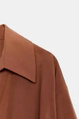 Camisa de lino color beige, con cuello solapa, escote en V y mangas largas. Presenta un diseño de bajo asimétrico con pliegues delanteros que generan un efecto abullonado.
