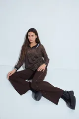 Pantalón de denim corte wide leg color marrón, con ruedo desflecado y detalle de tachas metálicas a lo largo de las costuras laterales.