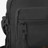 Morral pequeño tipo bandolera de color negro, confeccionado en poliamida. Cuenta con un compartimento principal con cierre de cremallera, un bolsillo frontal con cierre, correa de hombro ajustable y un pequeño detalle circular con logo en la parte inferior.
