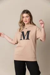 Remera gris con estampa de la letra M en negro y cadena plateada en el cuello.