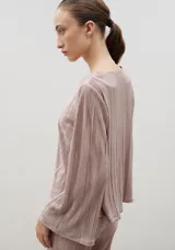Blusa plisada de color crema con escote en V y mangas largas ligeramente acampanadas. Presenta una textura plisada en toda la prenda que aporta caída y movimiento.