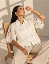 Camisa blanca de manga corta con diseño floral bordado y calado, cuello camisero y cierre frontal de botones.