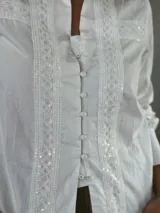 Camisa negra con cuello alto, mangas largas abullonadas y cierre frontal con botones. Presenta detalles de encaje y lentejuelas en el frente.