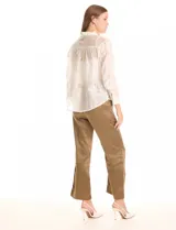 Camisa de tencel color blanco roto, semitransparente, con bordados florales en blanco. Tiene cuello con solapa, cierre frontal con botones decorados y un bolsillo en el pecho.