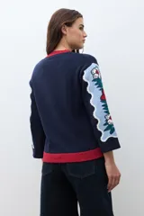 Sweater de punto color azul marino con diseño jacquard floral en las mangas y detalle de cuello redondo en color rojo. Presenta un corte holgado y mangas tres cuartos.