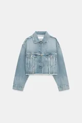 Chaqueta crop de denim azul claro con cuello solapa, manga larga con puño y bolsillos de plastrón con solapa en el pecho. Presenta detalles de costuras deshilachadas y cierre frontal con botones metálicos.