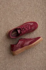 Zapatilla urbana de diseño clásico, color bordó, confeccionada en una combinación de cuero y gamuza. Presenta cordones al tono, suela de goma color caramelo y detalle de marca grabado en dorado en el lateral.