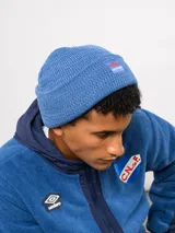 Gorro tipo beanie de tejido de punto color blanco crema, con parche frontal que incluye el logo de Umbro y la inscripción Nacional.