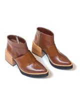 Botineta de cuero negro con diseño combinado en cuero charolado, plataforma y taco cuadrado de madera clara. Presenta cierre lateral y puntera redondeada.