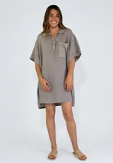 Camisola de lino color gris topo, estilo túnica o vestido corto, con cuello polo abotonado y manga corta ancha. Presenta un bolsillo frontal con detalle de perforaciones circulares.