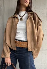 Campera tipo bomber de gamuza con diseño relajado, cierre frontal, cuello camisero y detalles de apliques en los hombros.