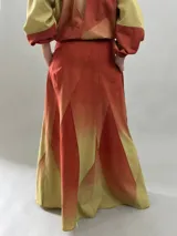 Falda larga de lana con diseño de paneles geométricos y efecto degradado que transiciona de verde esmeralda a tonos amarillentos. Presenta cintura alta, cierre invisible lateral y bolsillos ocultos.