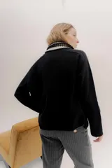 Polera tejida en lambswool color beige, con cuello alto y diseño de intarsia en tonos marrones y grises. Presenta botones forrados en el cuello para modular la apertura.