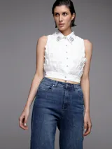 Camisa blanca sin mangas con cuello clásico, cierre frontal con botones y apliques de strass en cuello y frente.