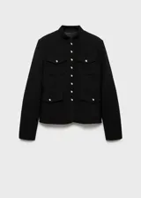 Chaqueta de estilo militar en color negro, con cuello redondo, manga larga y cierre frontal de botones metálicos dorados. Presenta cuatro bolsillos de solapa en la parte delantera y diseño de corte recto.