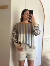 Sweater de tejido de punto con silueta oversize, cuello redondo y mangas largas abullonadas. Presenta un diseño patchwork con rayas verticales en tonos rojo, rosa y gris verdoso en el cuerpo, y un estampado floral en tonos rosa y rojo con detalles dorados en las mangas. Los puños y el cuello tienen un ribete a rayas horizontales.