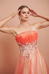 Vestido largo de fiesta, strapless, con busto drapeado y falda de tul con degradé de color coral a blanco. Presenta bordados florales en el corpiño.