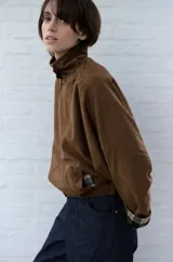 Campera de pana color marrón, con cuello alto y cierre frontal. Presenta un diseño holgado con mangas amplias y puños con detalle de forro a cuadros.