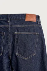 Pantalón de jean corte slim fit, color azul oscuro, con diseño de cinco bolsillos, tiro medio y cierre frontal con cremallera y botón.