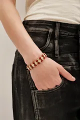 Pulsera de estilo étnico compuesta por cordón de algodón en color rojo y piezas metálicas cuadradas con textura en tono dorado.