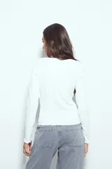 Remera de manga larga con ajuste al cuerpo, confeccionada en tejido acanalado de color marrón. Presenta cuello redondo y terminaciones con borde ondulado en puños y ruedo.