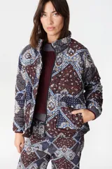Campera de abrigo con cuello alto y manga ranglan, confeccionada en tela capitoneada con relleno y forro interno. Presenta un diseño estampado con motivos geométricos y paisley en tonos azules y marrones.